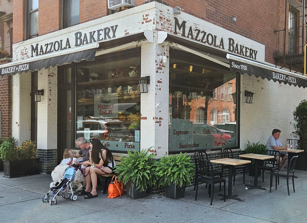 Mazzola Bakery storefront with outdoor seating area on a city street.